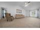 Bright living room with a tan carpet, a tan couch, a ceiling fan, and a big window with a view at 21425 Sw Plantation St, Dunnellon, FL 34431