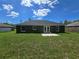 Back exterior featuring lush green grass, trees, and a cozy patio area at 235 Locust Pass Ln, Ocala, FL 34472