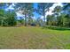 Spacious backyard with sheds, mature trees, and grassy area under a blue sky with scattered clouds at 23737 Nw Mallard Ave, Dunnellon, FL 34431