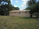 Backyard view of a beige home with a metal roof, sparse grass and mature trees, under a blue and partly cloudy sky at 2912 Ne 24Th Ct, Ocala, FL 34479