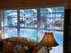 Relaxing living room view through blinds overlooking a sparkling pool and lush patio greenery at 3579 Sw Shorewood Dr, Dunnellon, FL 34431