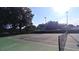 Outdoor tennis court featuring a pristine green surface and net, surrounded by trees and blue skies at 6070 Sw 98Th Loop, Ocala, FL 34476