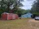 Exterior of home with red outbuilding on a large lot surrounded by mature trees at 10805 Se 102Nd Pl, Ocala, FL 34472