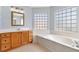 Main bathroom with double windows, soaking tub, tiled floors, and wood cabinets at 17902 Se 115Th Cir, Summerfield, FL 34491