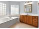 Main bathroom showcasing a soaking tub, wood cabinets, tile flooring, and glass block windows at 17902 Se 115Th Cir, Summerfield, FL 34491
