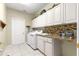 Bright laundry room features tile floors, granite counters, washer, dryer, sink, and white cabinets at 13885 Del Webb Blvd, Summerfield, FL 34491