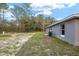 View of backyard with grass and sand surrounded by trees and gray house with windows at 23163 Nw Shamrock Ave, Dunnellon, FL 34431