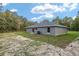 Side view of backyard with grass and sand surrounded by trees and a gray house with windows at 23163 Nw Shamrock Ave, Dunnellon, FL 34431