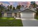 Home exterior featuring a gray house, front door, and garage with a concrete driveway and green grass at 23163 Nw Shamrock Ave, Dunnellon, FL 34431