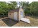 Outdoor shed with a roll-up door and a standard entry door, set against a backdrop of lush greenery and a wooden fence at 11447 Sw 128Th Ave, Dunnellon, FL 34432