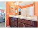 Bathroom with orange walls featuring double vanity with dark wood cabinets and dual sinks at 3500 Countryside Path, The Villages, FL 32163