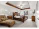 This primary bedroom offers a sleek ceiling fan, accent beams, and hardwood sleigh bed, with plush patterned chaise lounge at 907 Trifu Ter, The Villages, FL 32163