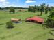 Aerial shot of a property featuring a red barn, car port, and expansive green pastures surrounded by mature trees at 2540 Ne 120Th St, Anthony, FL 32617