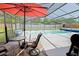 A table with a red umbrella sits on the patio next to a sparkling blue swimming pool at 6211 Se 126Th St, Belleview, FL 34420