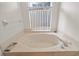 A luxurious, neutral-toned bathtub with jacuzzi jets and chrome fixtures sits below a window with white blinds at 10716 Sw 53Rd Cir, Ocala, FL 34476