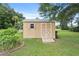 Exterior view of tan storage shed in green lawn with white trim and double doors at 10716 Sw 53Rd Cir, Ocala, FL 34476