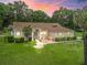 Stunning single-story home with a well-manicured lawn, mature trees, and charming front patio at dusk at 16 Count Fleet Dr, Ocala, FL 34482