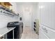Modern laundry room with black appliances, overhead shelving, and custom laundry door at 6046 Sw 86Th Cir, Ocala, FL 34481