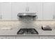 Close up of cooktop with white cabinets, gray counters, and backsplash at 9577 Sw 82Nd Street Rd, Ocala, FL 34481