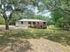 Ranch-style home with a wooden deck, set amidst mature trees and a serene, shaded lawn at 2580 Se 157Th Lane Rd, Summerfield, FL 34491