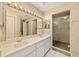 Bathroom featuring dual sinks, a large mirror with Hollywood lights, and a glass-enclosed shower at 9001 Sw 91St Cir, Ocala, FL 34481