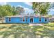 Backyard view of a blue home with a concrete patio, surrounded by green grass and mature trees at 11 Se Fir Trail Trak, Ocala, FL 34472
