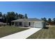 Single-story home with an attached garage and a long driveway, surrounded by lush trees and a clear blue sky at 14443 Sw 21St Pl, Ocala, FL 34481
