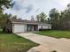 Single-story home with an attached garage, a red front door, lawn and two chairs on the front porch at 120 Fisher Ct, Ocklawaha, FL 32179
