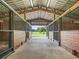 View of the interior of the horse barn with metal roof, wooden stall partitions, and open view to outside at 402 Sw 127Th Pl, Ocala, FL 34473