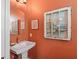 Quaint powder room with decorative framed window, pedestal sink, and coral painted walls at 402 Sw 127Th Pl, Ocala, FL 34473