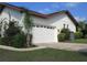 Attached two-car garage with white door framed by vibrant tropical landscaping at 8770 Sw 196Th Terrace Rd, Dunnellon, FL 34432