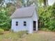 Exterior view of the white shed showcasing its simple design and garden setting, surrounded by foliage and greenery at 1610 Se 22Nd Ave, Ocala, FL 34471