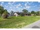 Sprawling front lawn of a single-story home with painted wood paneling and mature landscaping under a partially cloudy sky at 5720 Se 20Th St, Ocala, FL 34480