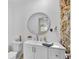Bathroom features a circular mirror, stone accent wall, and white vanity at 2922 Cocovia Way, Leesburg, FL 34748