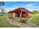Red outbuilding with a covered patio, grill, bench, and green lawn at 6497 W Anthony Rd, Ocala, FL 34479
