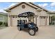 Beige single-Gathering home featuring a driveway with a golf cart parked in front of the two-car garage at 12169 Se 172Nd Ln, Summerfield, FL 34491