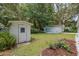 The backyard boasts a manicured lawn, a white storage shed, and a cozy patio area with umbrella and lounge chairs at 12335 Se 130Th Ct, Ocklawaha, FL 32179