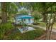 Charming home with a cozy outdoor seating area under a blue umbrella, surrounded by lush landscaping and mature trees at 12335 Se 130Th Ct, Ocklawaha, FL 32179