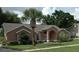 Inviting single-story home featuring a beautiful palm tree, arched entryway, and lush green lawn at 14126 Greater Pines Blvd, Clermont, FL 34711