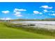 Picturesque lake view with a wooden dock, surrounded by green grass and lily pads beneath a clear blue sky with fluffy clouds at 3000 Pine Grove Ln, Lady Lake, FL 32159