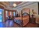 Relax in this main bedroom featuring a tray ceiling, chandelier, hardwood floors, and a four-poster bed at 695 Se 47Th Loop, Ocala, FL 34480