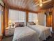 Cozy bedroom featuring wood-paneled walls, two twin beds with nightstands, and lots of natural light from two windows at 5915 Se Holly Rd, Belleview, FL 34420