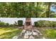 Backyard view featuring a brick fire pit and white vinyl fence surrounded by lush greenery at 3515 Ne 43Rd Pl, Ocala, FL 34479