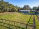 Fenced paddock leading to a blue and white horse barn set amongst green pastures and mature trees at 7563 Nw 21St St, Ocala, FL 34482