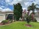 Landscaped front yard features lush green grass, palm trees, flowering shrubs, and an inviting facade with screened entry at 611 Allenwood Loop, The Villages, FL 32162