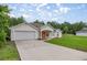 An exterior shot of a one-story home with a two-car garage and a spacious driveway, surrounded by a verdant lawn at 144 Malauka Pass, Ocklawaha, FL 32179
