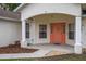 Inviting front porch featuring decorative columns, a coral-colored door, and lush landscaping provides a warm welcome at 144 Malauka Pass, Ocklawaha, FL 32179