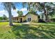 A spacious, grassy backyard with lush trees, leading up to a charming yellow home and patio area, perfect for outdoor enjoyment at 3831 Se 48Th St, Ocala, FL 34480
