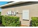 Side view of a house showcasing a Tesla Powerwall with electrical boxes and lush green bushes at 5093 Nw 35Th Lane Rd, Ocala, FL 34482
