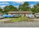 Beige single-story house with a brown front door and an unkept yard with an array of vehicles at 2508 India Palm Dr, Edgewater, FL 32141